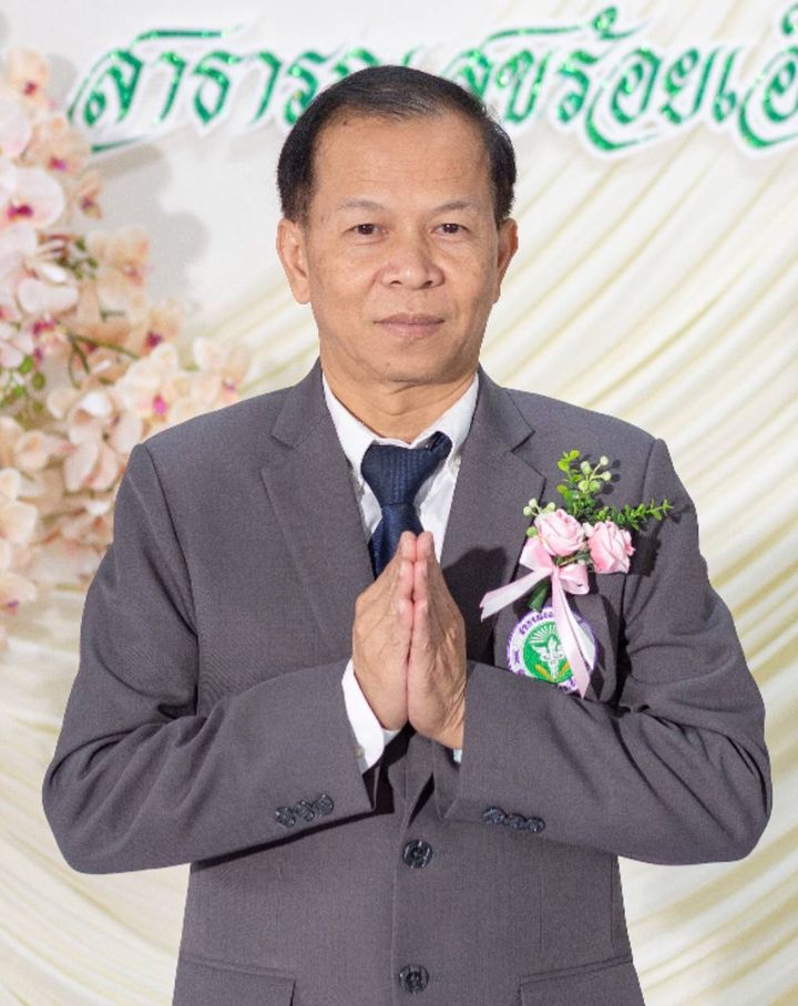นายวุฒิพงศ์ ในสูทสีเทาติดดอกไม้ ไหว้สวัสดี